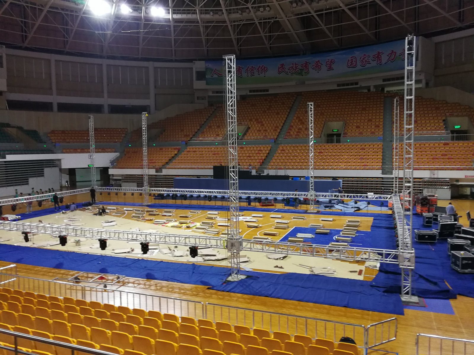 体育馆桁架舞台搭建现场：蓝色地胶与金属桁架结构全景
