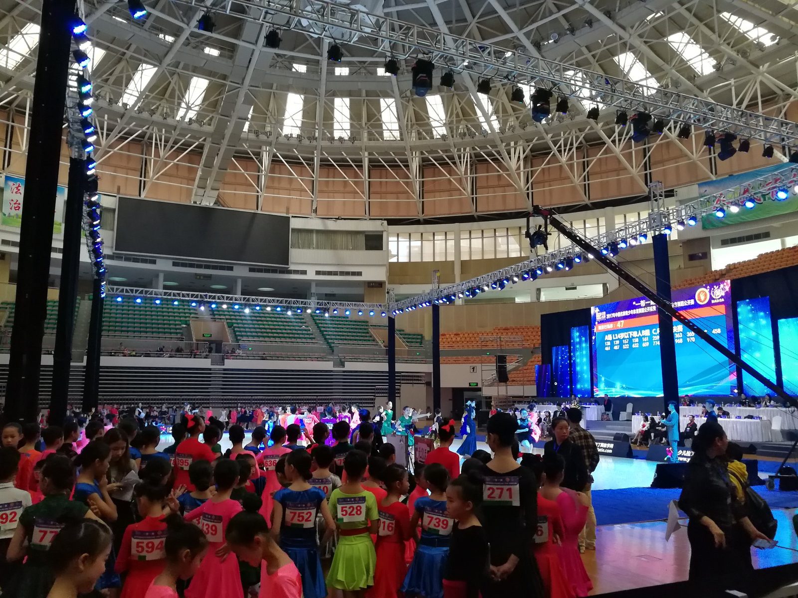 大型体育馆发布会现场：桁架吊装灯光大屏、巨型 LED 主屏与上千观众方阵