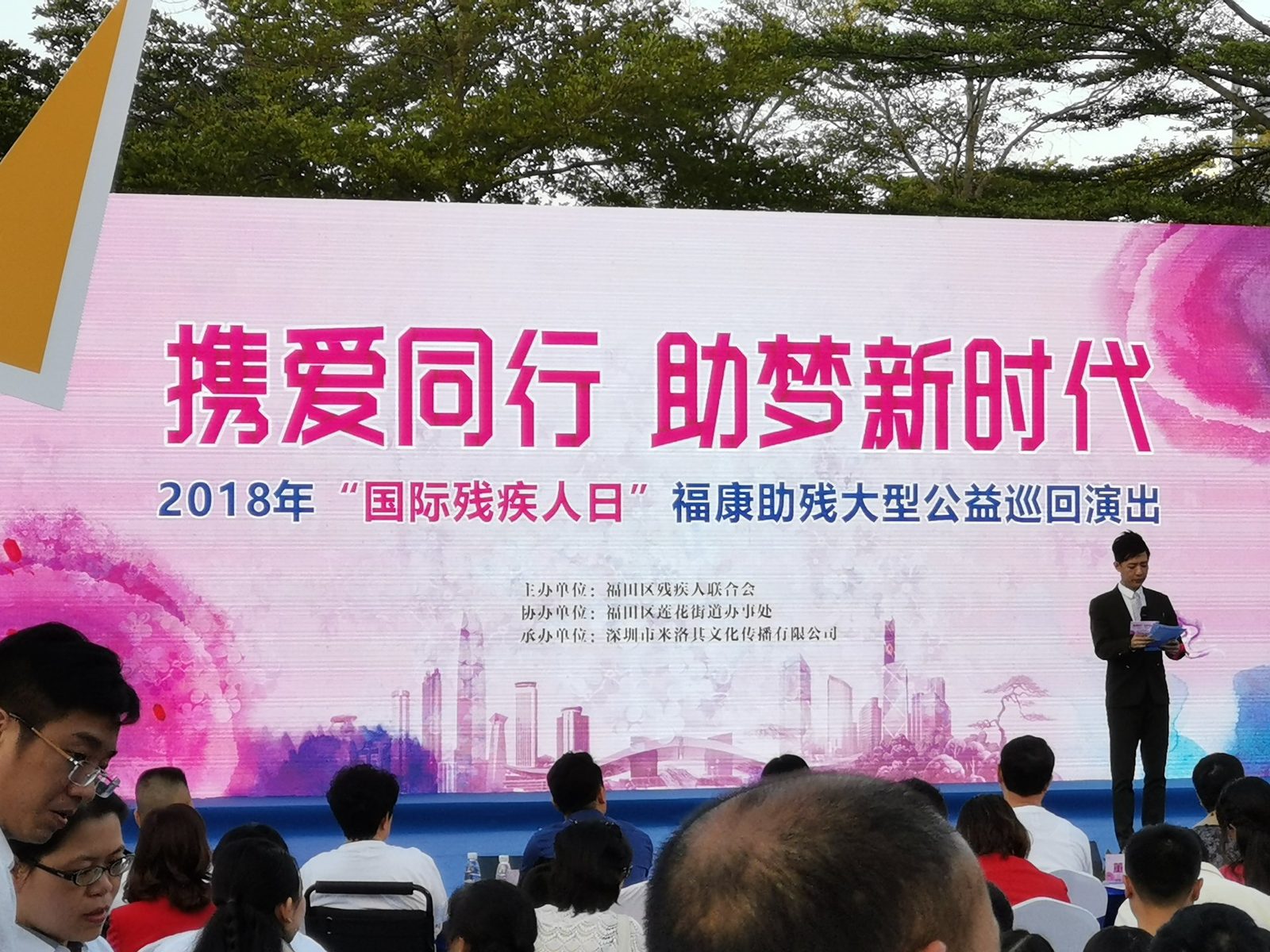 公益活动现场：主持人站在大型粉色主视觉舞台前