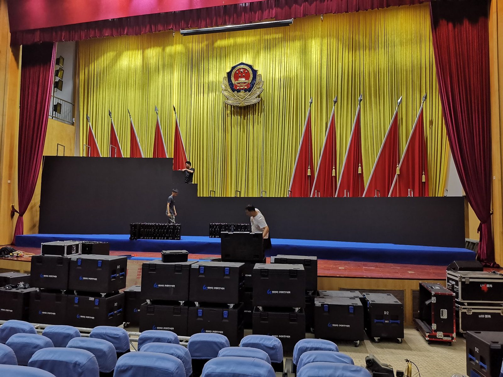 政府礼堂律所行业活动搭建现场：红黄舞台幕布与大量 LED 设备航空箱进场