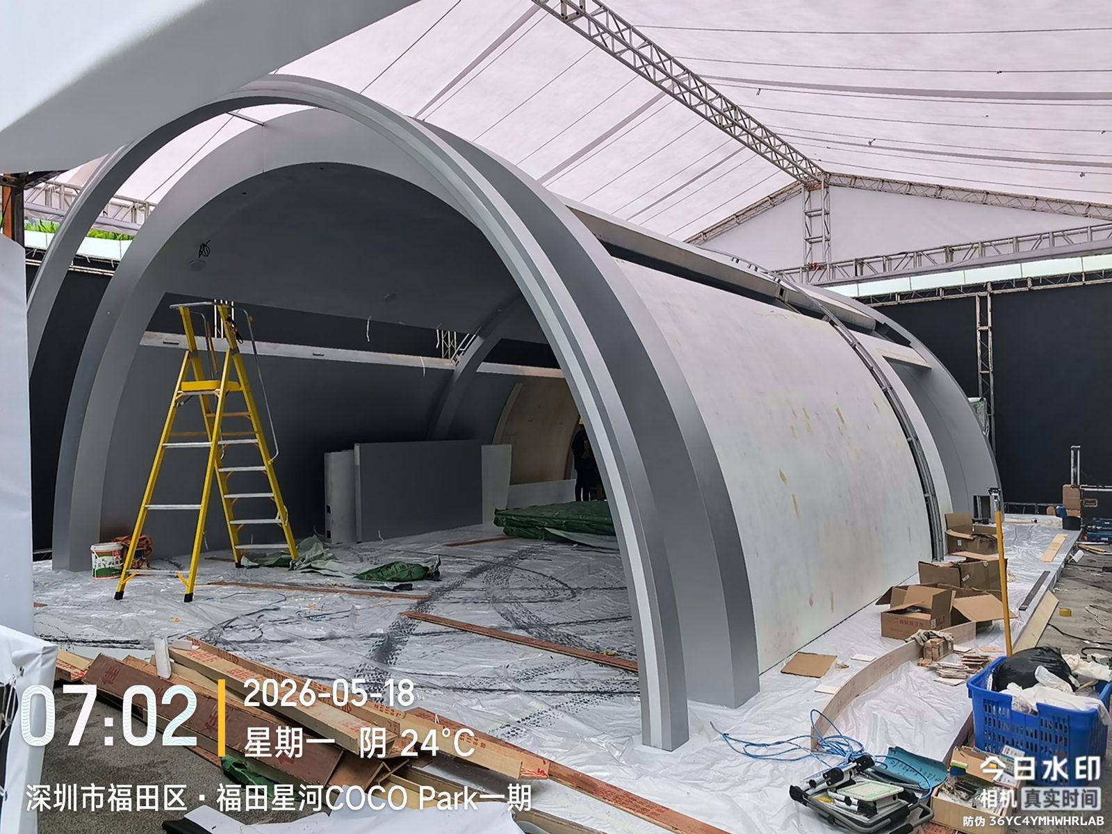 户外展台搭建现场：白色弧形拱门结构与搭建梯子作业中