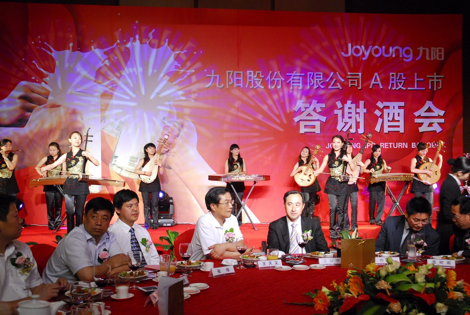 九阳股份 A 股上市答谢酒会圆桌宴席现场：红色主题背景板、民族乐器暖场表演与答谢宴