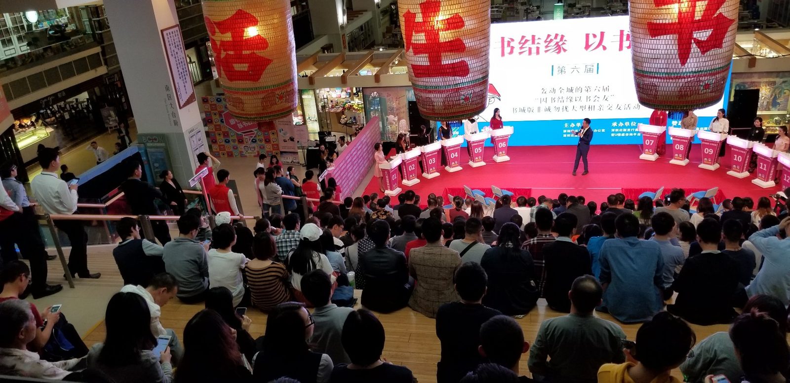 大型互动活动现场：商城中庭观众围坐观看红色主舞台上的互动游戏环节